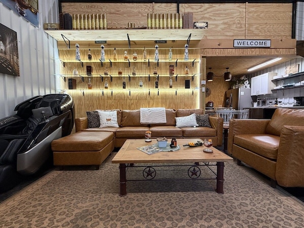 A cozy living room with leather sofas, a coffee table, and a wall display of various bottles.