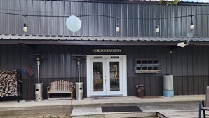 Un bâtiment rustique à l’extérieur métallique, avec un banc en bois, une poubelle et une pancarte sur laquelle on peut lire : « SOYEZ LES BIENVENUS ».