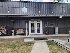 A rustic building with a metal exterior, a wooden bench, a trash can, and a sign that reads 'BE OUR GUEST.'