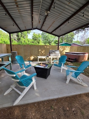 An outdoor patio with a grill, fire pit, and Adirondack chairs.