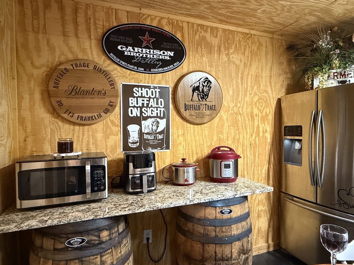 A kitchen with wooden barrel countertops, a microwave, a coffee maker, a red slow cooker, and a refrigerator.