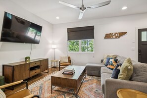 Ein modernes Wohnzimmer mit Flachbildfernseher, Deckenventilator, Sofa, Couchtisch und Holzschrank.