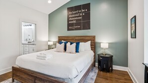 Een keurig opgemaakt slaapkamer met een groot bed, een nachtkastje, een spiegel en een citaat op de muur.