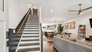 Een modern interieur met een trap naar een eethoek, een woonkamer met een bank en een plafondventilator.