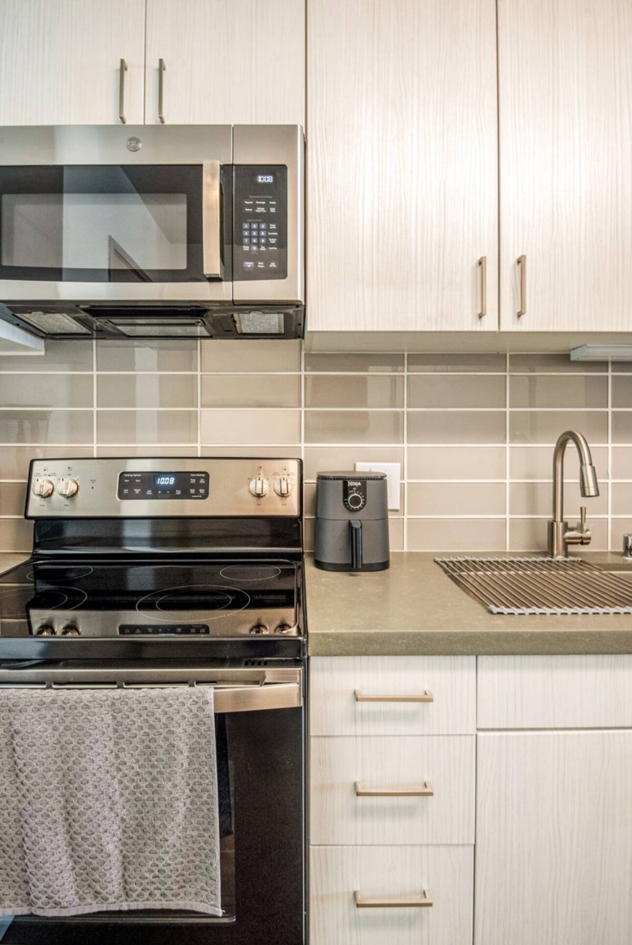 Una cocina moderna con electrodomésticos de acero inoxidable, microondas, horno, cafetera y un lavamanos con grifo.