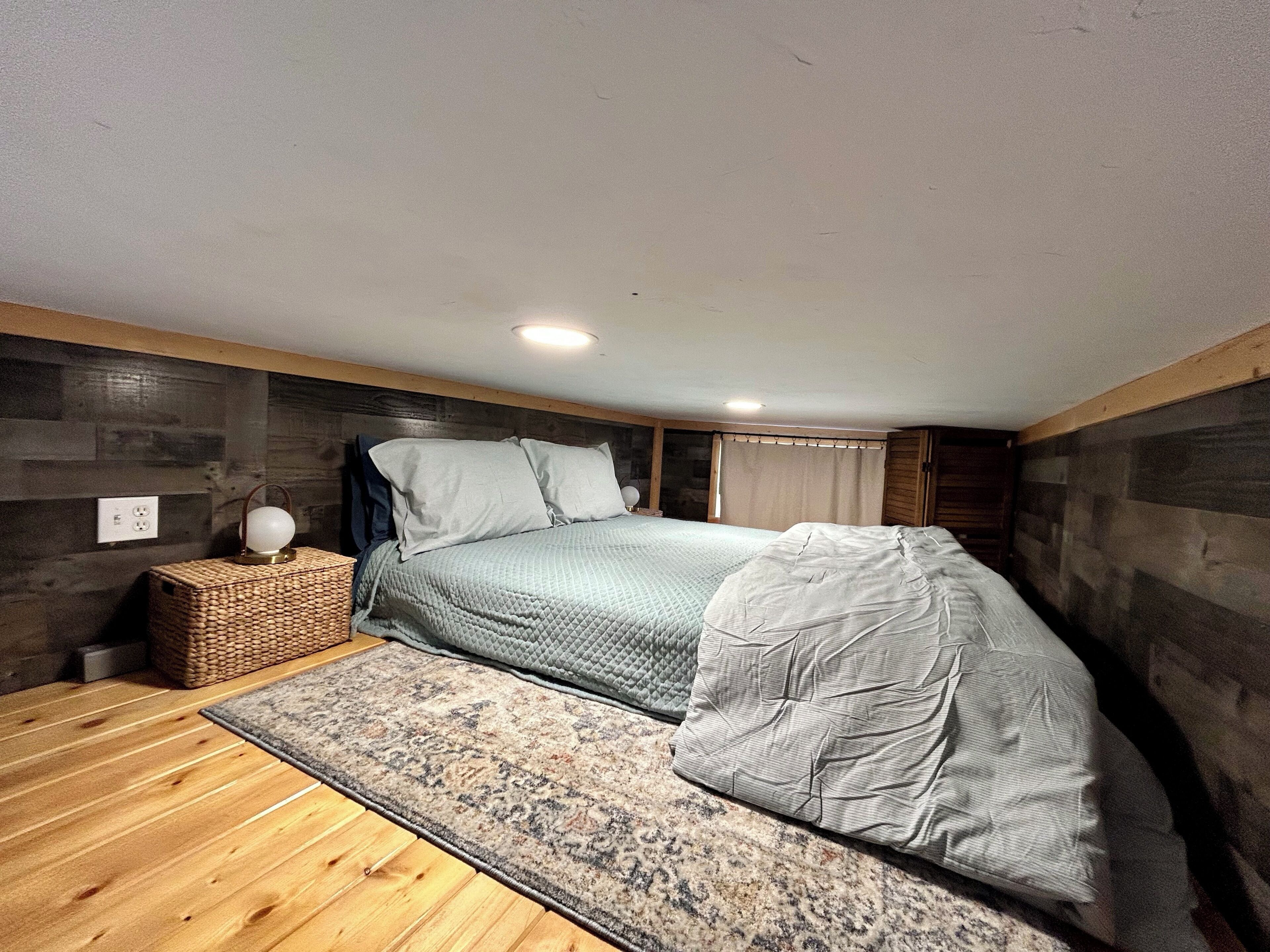 Een slaapkamer met een bed, nachtkastje, lamp en een raam met gordijnen.