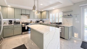 A modern kitchen with marble countertops, green cabinets, and stainless steel appliances.
