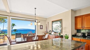 A kitchen with a large island, wooden cabinets, and a view of the ocean. - Makena Surf G-201 - Corner Unit With Amazing Views, Pools, Pickleball & Peloton (Kihei)