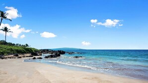 A beach with clear blue water, sandy shore, and a distant mountain. - Makena Surf G-201 - Corner Unit With Amazing Views, Pools, Pickleball & Peloton (Kihei)