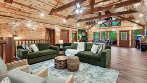 A spacious log cabin interior with two green sofas, a round wooden table, and a fluffy rug. - Cabin in Sevierville Sleeps 28 Pool Hot Tub (Sevierville)