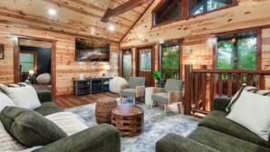 A cozy cabin interior with wooden walls, a fireplace, comfortable seating, and large windows. - Cabin in Sevierville Sleeps 28 Pool Hot Tub (Sevierville)