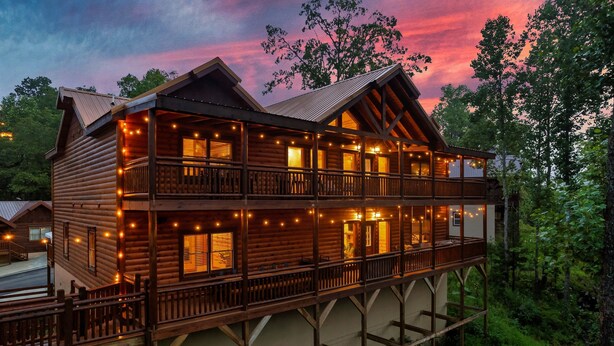 A log cabin with a balcony and multiple windows, surrounded by trees. - Cabin in Sevierville Sleeps 28 Pool Hot Tub (Sevierville)