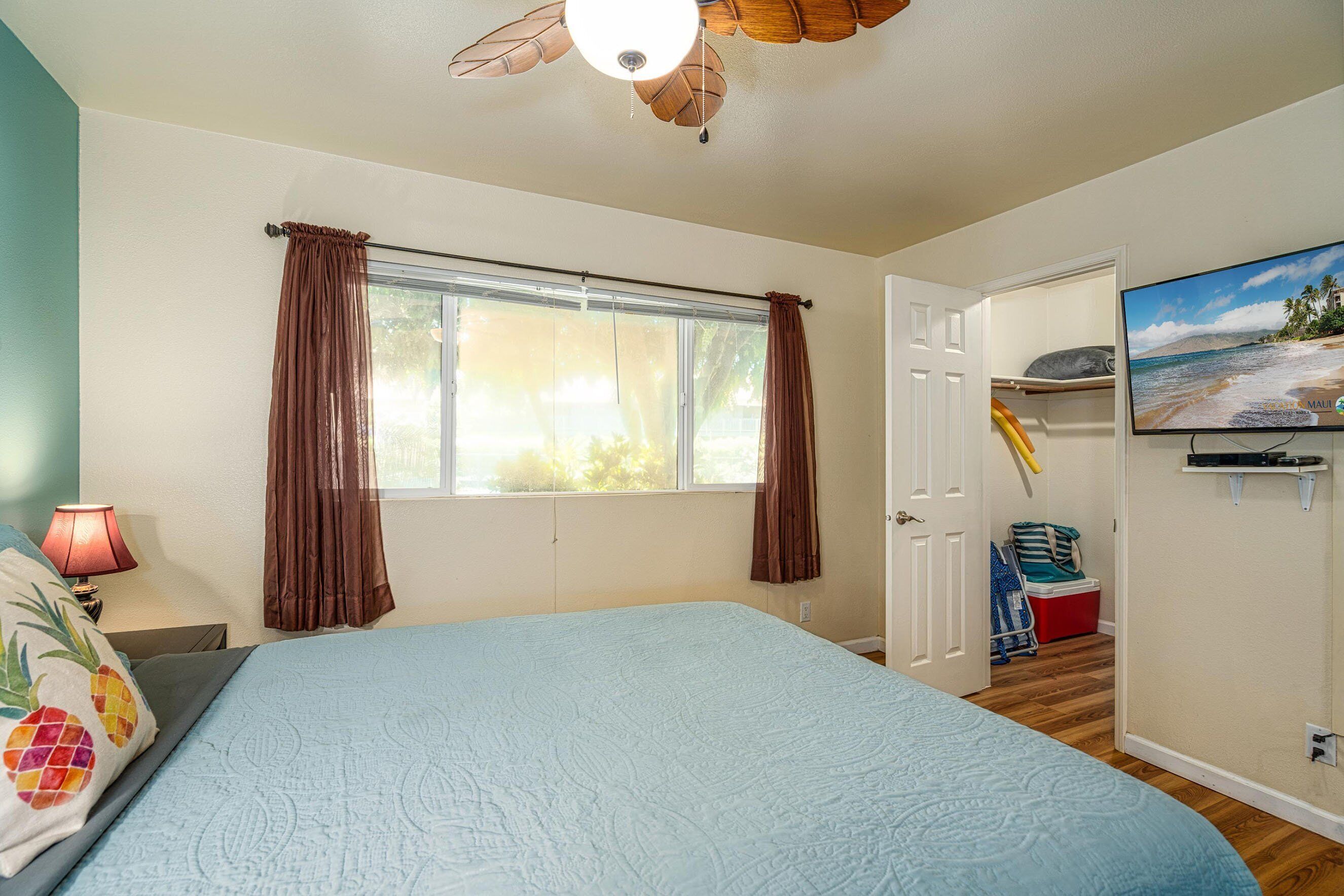 A bedroom with a bed, a ceiling fan, a window with curtains, a television, and a door leading to another room.
