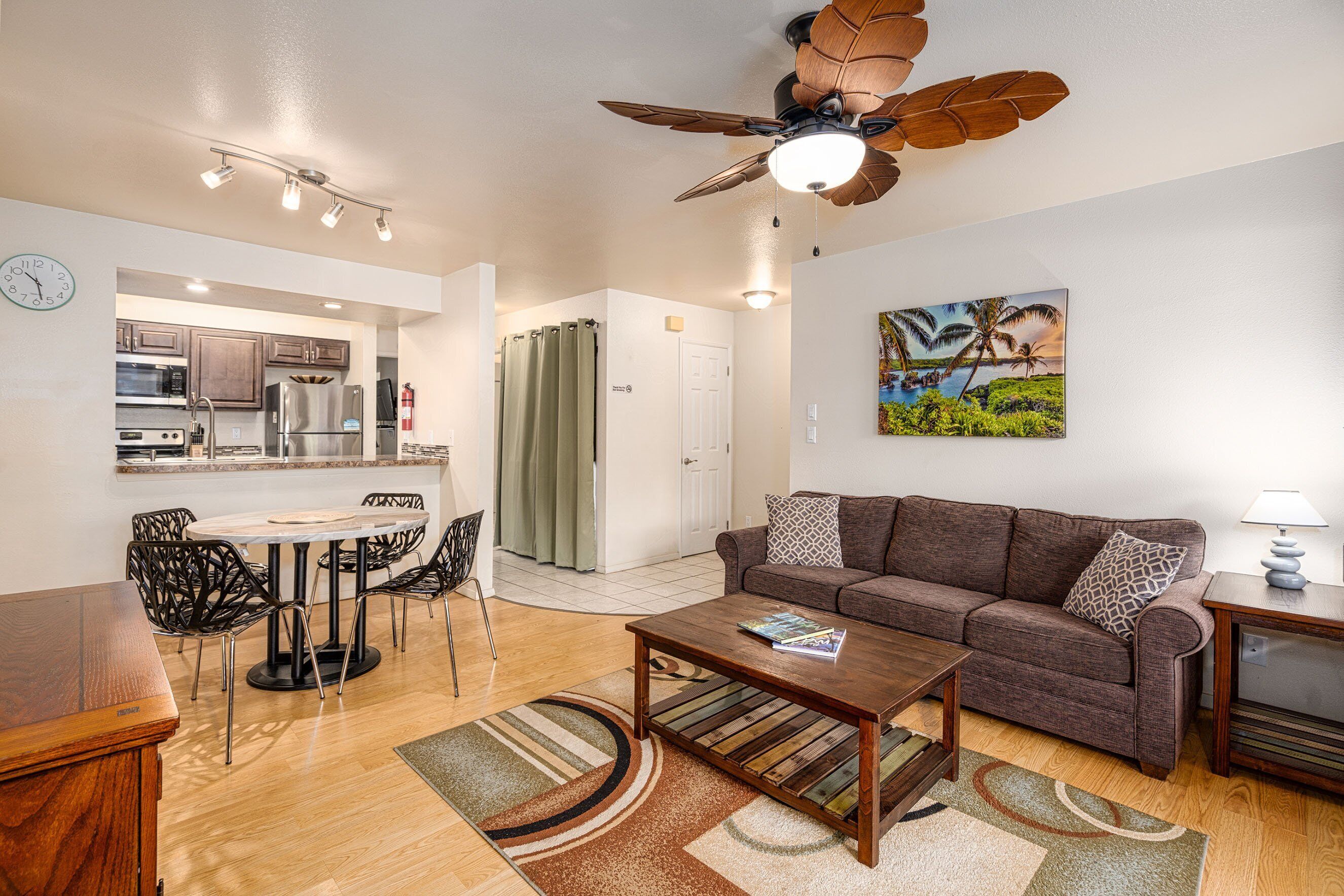 A modern living room with a brown sofa, a wooden coffee table, and a dining area with a white table and chairs.