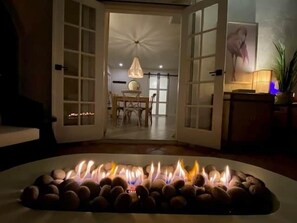 Una habitación con chimenea de piedra, una zona de comedor con sillas y una mesa, y un ventanal con vistas.