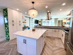 Une cuisine moderne avec des meubles blancs, un îlot central, un lustre et une hotte de cuisinière en acier inoxydable.