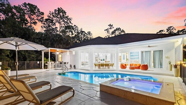 Un área de piscina moderna con jacuzzi, sillones de descanso y un patio cubierto.