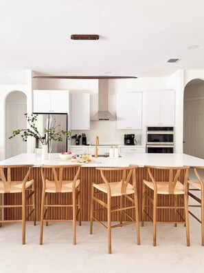 Een moderne keuken met een groot schiereiland, witte kasten en houten stoelen.