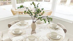 Un tavolo da pranzo rotondo apparecchiato per sei persone, con piatti bianchi e posate, circondato da sedie color beige.