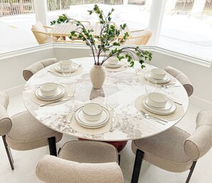 A round dining table set for six with white plates and silverware, surrounded by beige chairs. - Naples FL | Heated Pool Spa Pickleball Mini Golf (Naples)