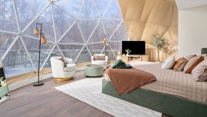 Un dormitorio moderno con una cama grande, un televisor y vistas a través de un ventanal geométrico.
