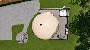 Vista aérea de un espacio exterior moderno con una gran estructura en forma de cúpula, una terraza de madera y una zona de estar con mesas y sillas.