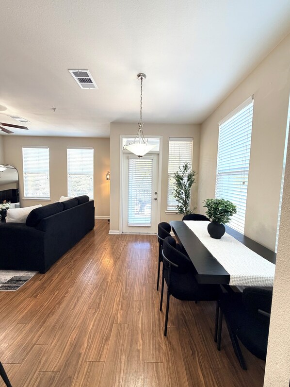 Una sala de estar moderna con un sofá negro, una mesa de comedor con sillas y una planta en maceta.