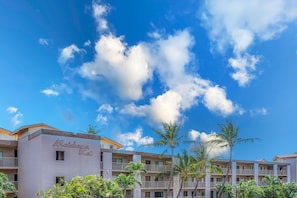 Un hotel con un letrero con su nombre, varios balcones y palmeras.