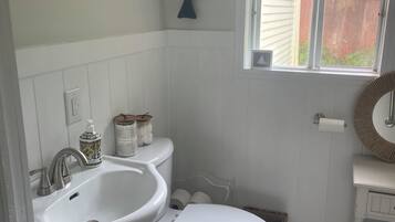 Un baño con lavamanos, inodoro y ventana blancos.
