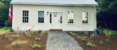 A white building with a metal roof, a flag, and a gravel path leading to the entrance.