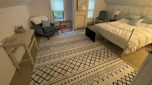 Un dormitorio con cama, una silla, un escritorio, una ventana y un tapete estampado.