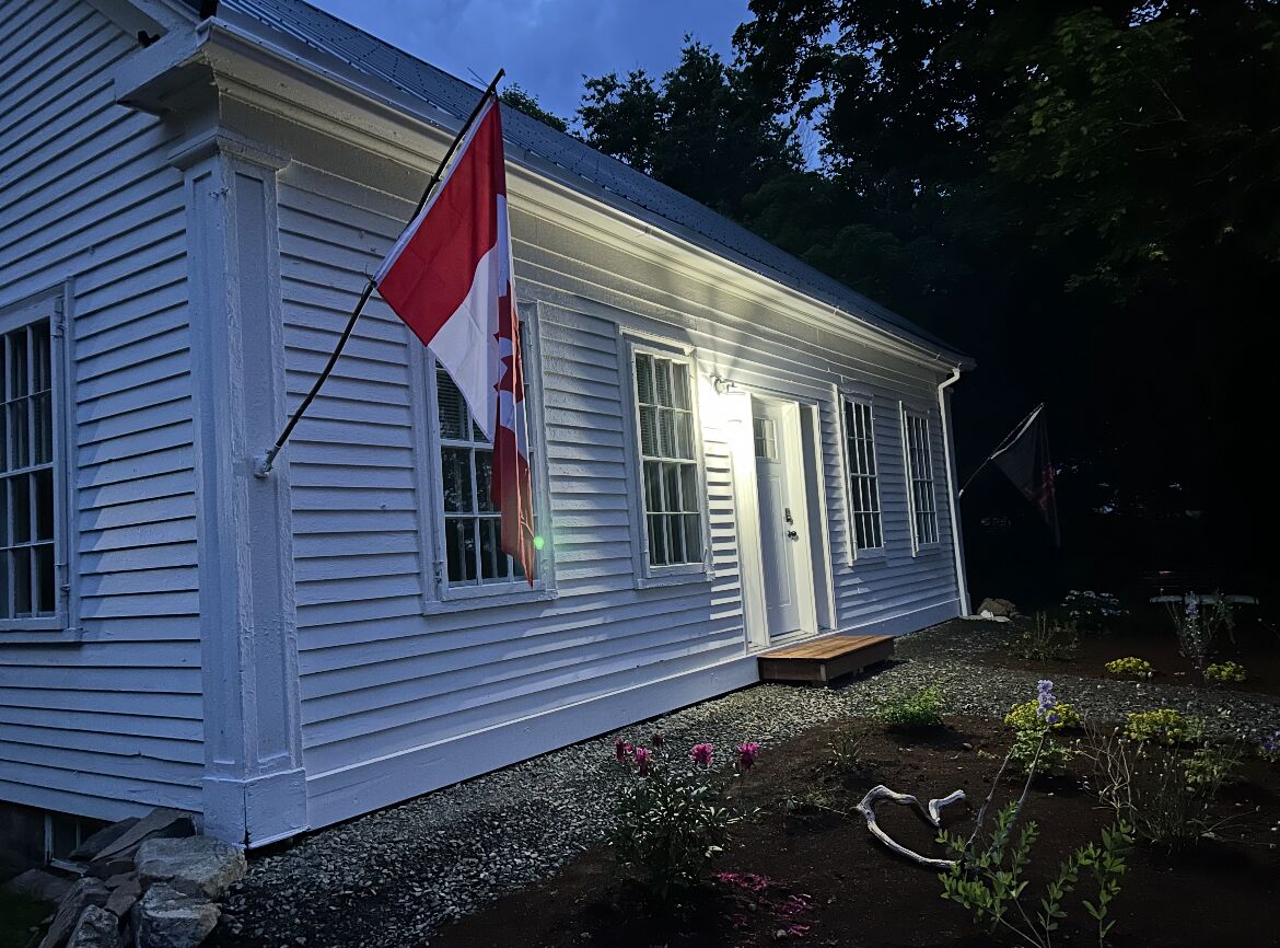 Una casa blanca amb una bandera, un jardí amb flors i un estany.