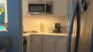Cocina compacta con armarios blancos, microondas, tostadora y cafetera.
