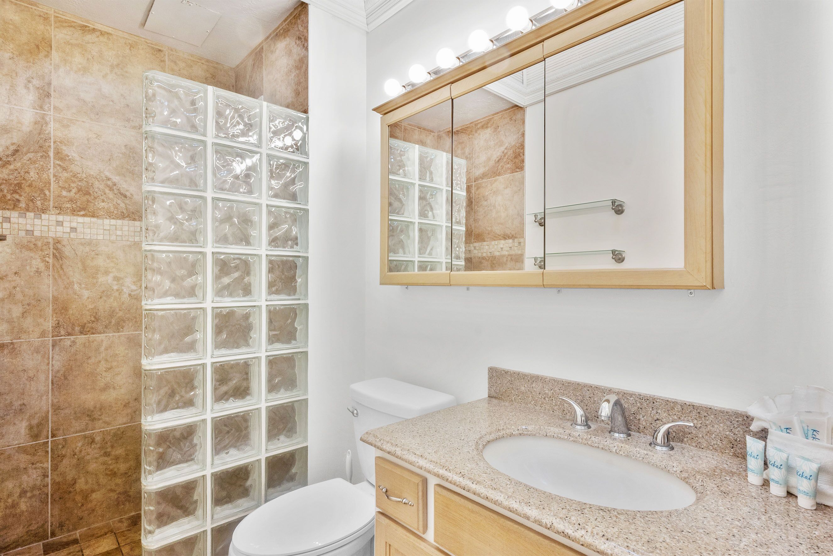 A bathroom with a large glass shower enclosure, a vanity with a sink and mirror, and toiletries on the counter.