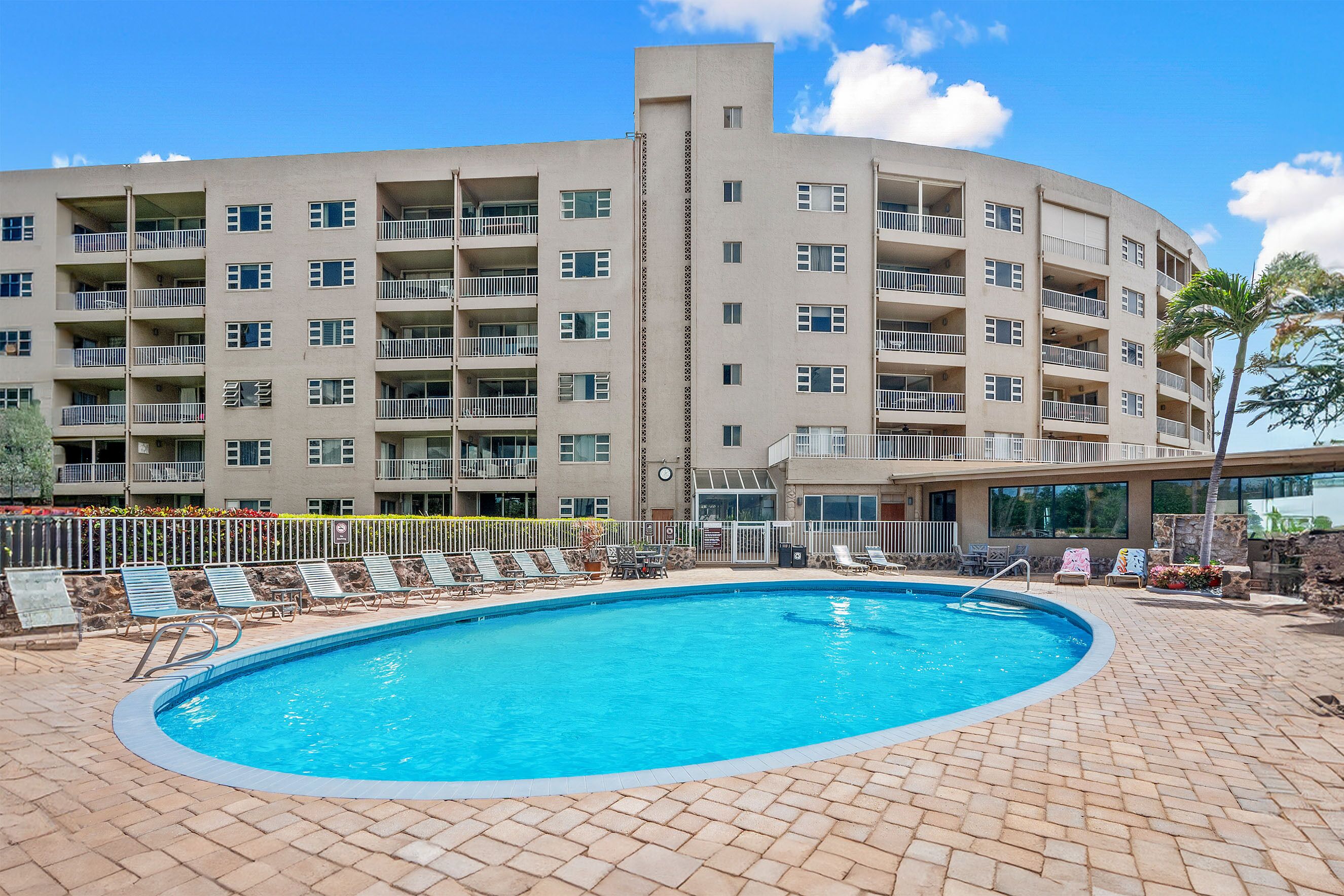 A hotel with a swimming pool, multiple balconies, and a brick-paved area.