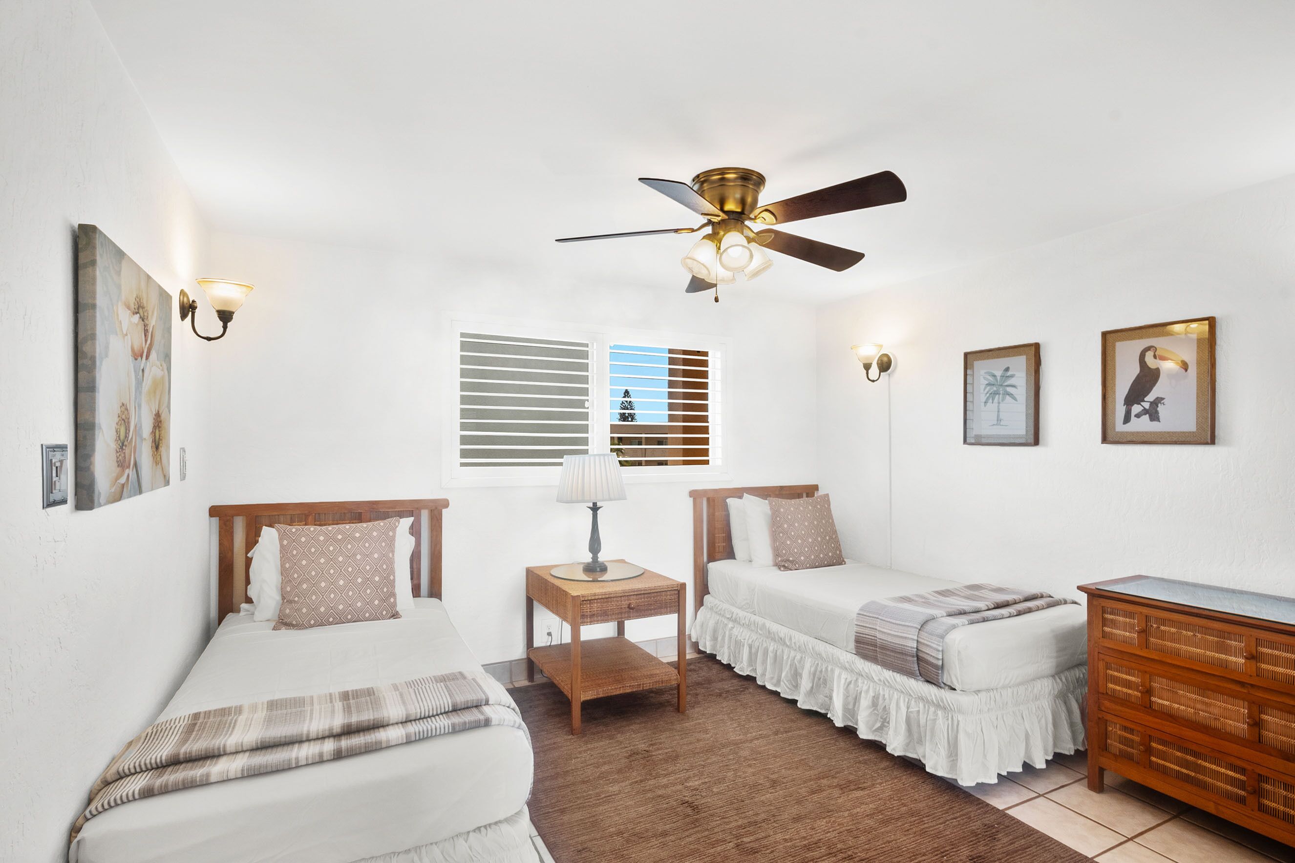 A bedroom with two single beds, a ceiling fan, a nightstand with a lamp, and a dresser.