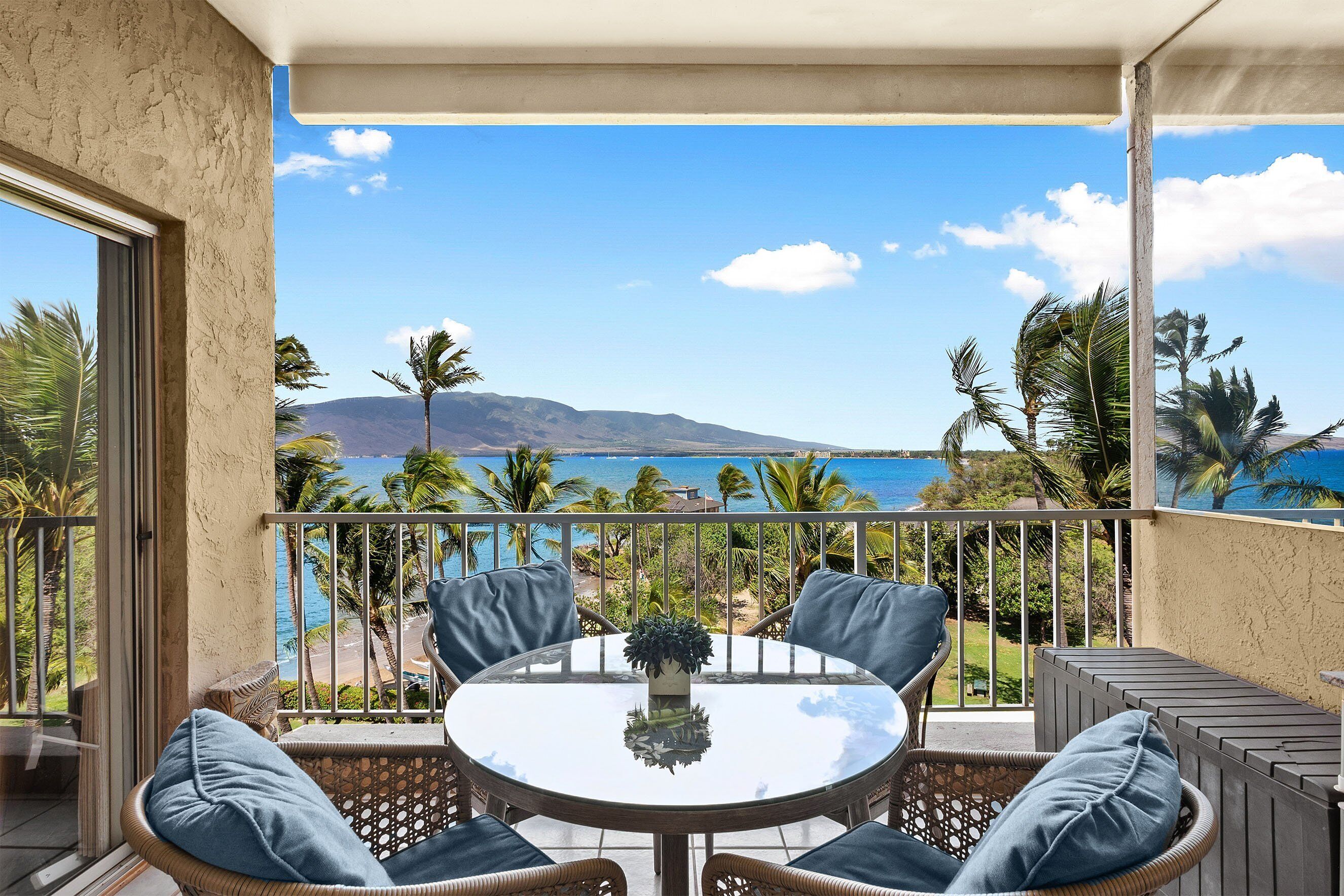Een balkon met een ronde tafel en stoelen, met uitzicht op een strand en de oceaan.