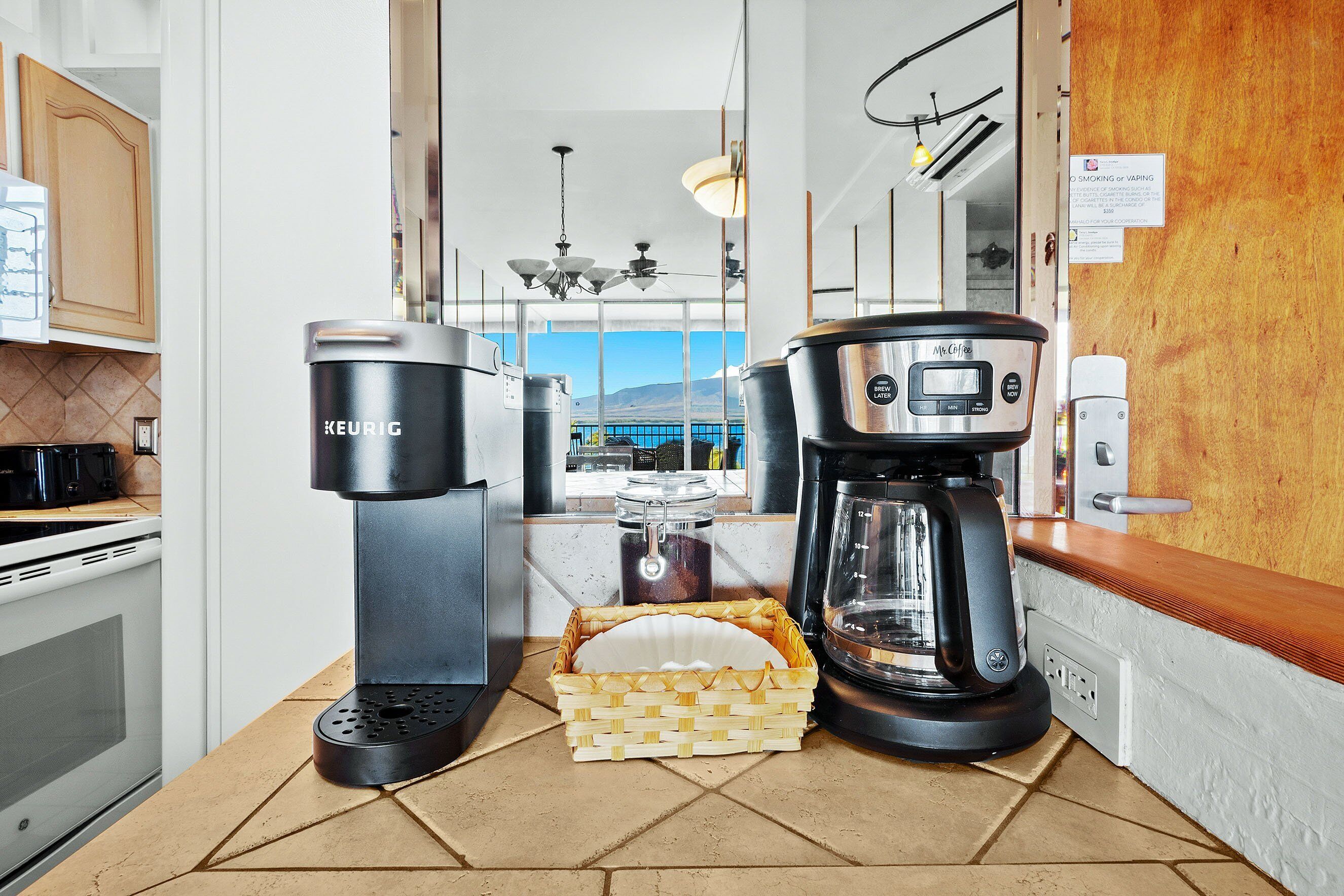 A modern kitchen with a Keurig coffee maker, a coffee pot, and a basket of paper plates.