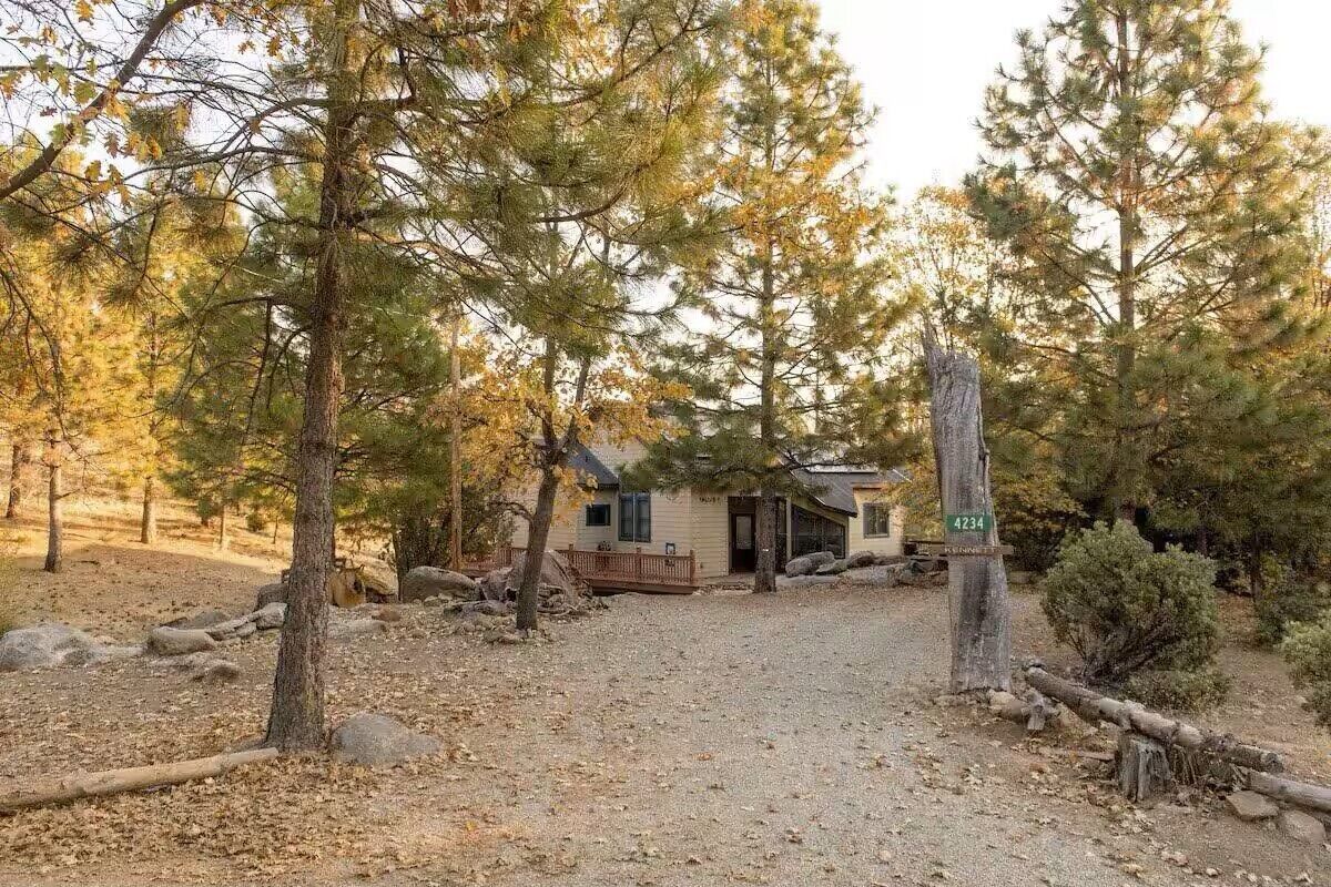 A cabin with a gravel driveway, surrounded by trees and rocks.
