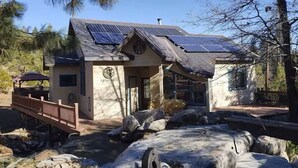 Una cabaña con fachada de piedra, paneles solares, una terraza de madera y una fuente de piedra.