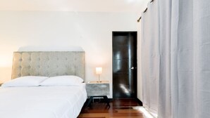 Ein Schlafzimmer mit einem Bett, einem Nachttisch, einer Lampe, einer Tür und einem Vorhang.