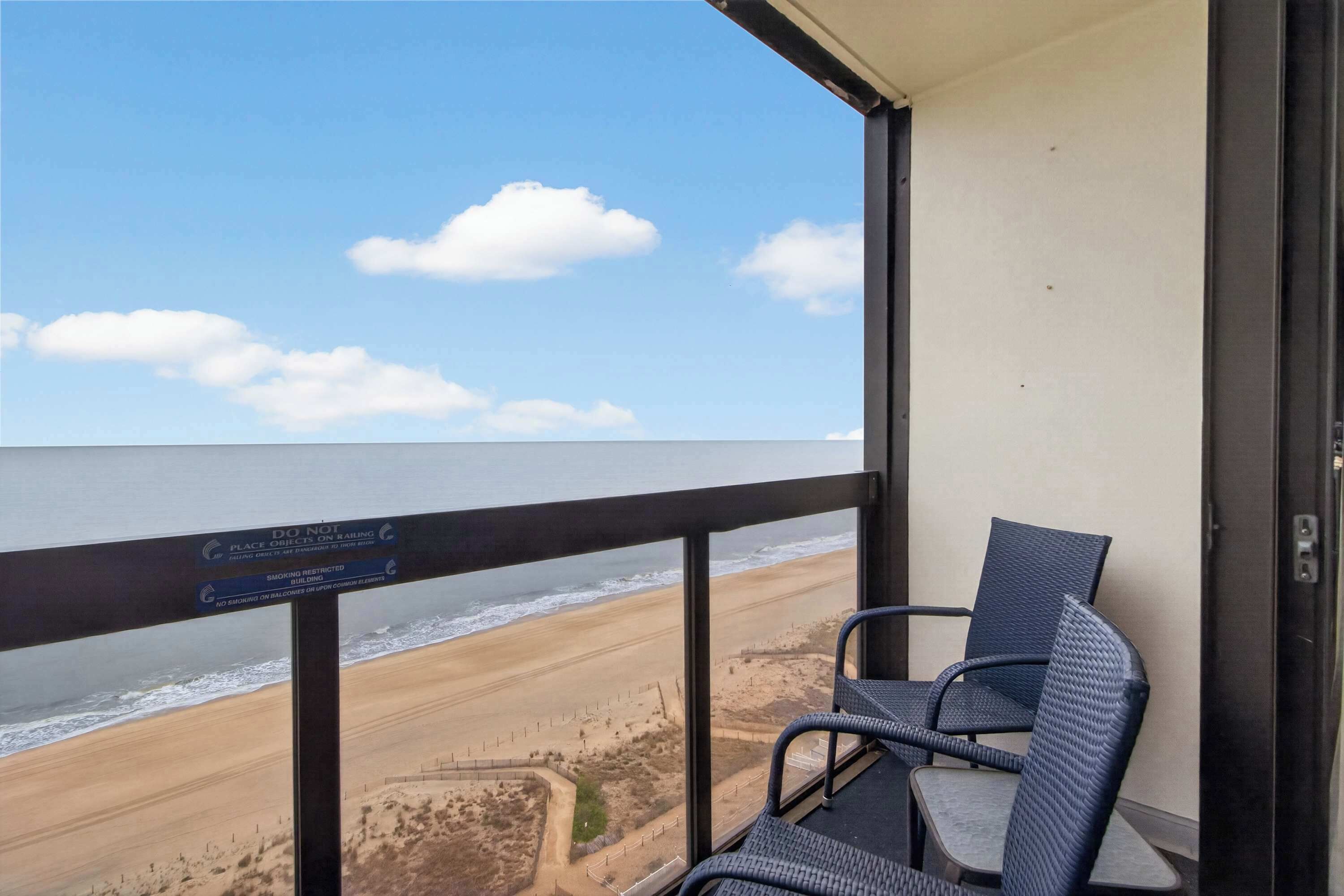 A balcony with a view of the beach, a sign indicating no smoking, and two wicker chairs.