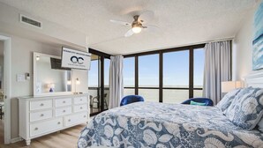 A bedroom with a large bed, a dresser, a chair, and a view of the ocean. - Golden Sands 1412, Oceanfront, Pools, Games (Ocean City)