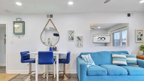 Un salon moderne avec un canapé bleu, un coin repas avec une table blanche et des chaises bleues, et un grand miroir accroché au mur.
