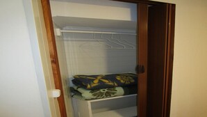 Un armadio con asta appendiabiti ed mensole, contenente coperte piegate e un cuscino.