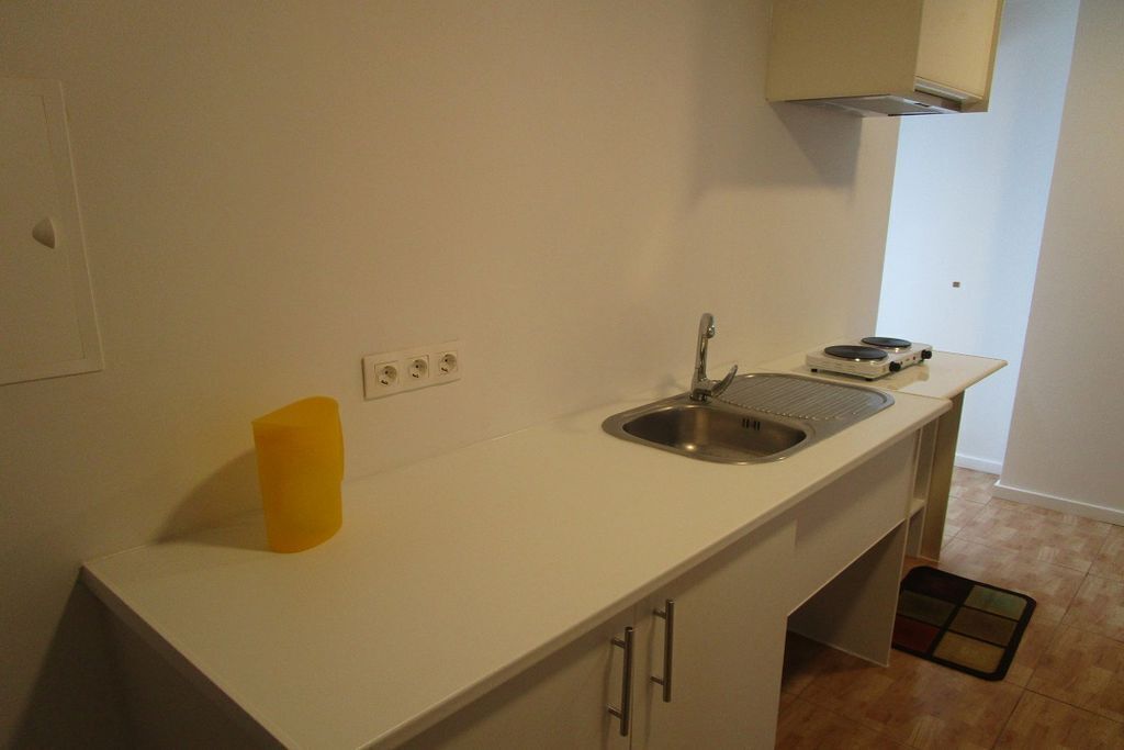 Een kleine keuken met een spoelbak, een gele bekerhouder en een fornuis.
