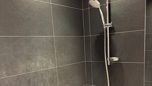 Un baño moderno con paredes revestidas de baldosas oscuras, una bañera blanca y una ducha con cabezal de ducha manual.