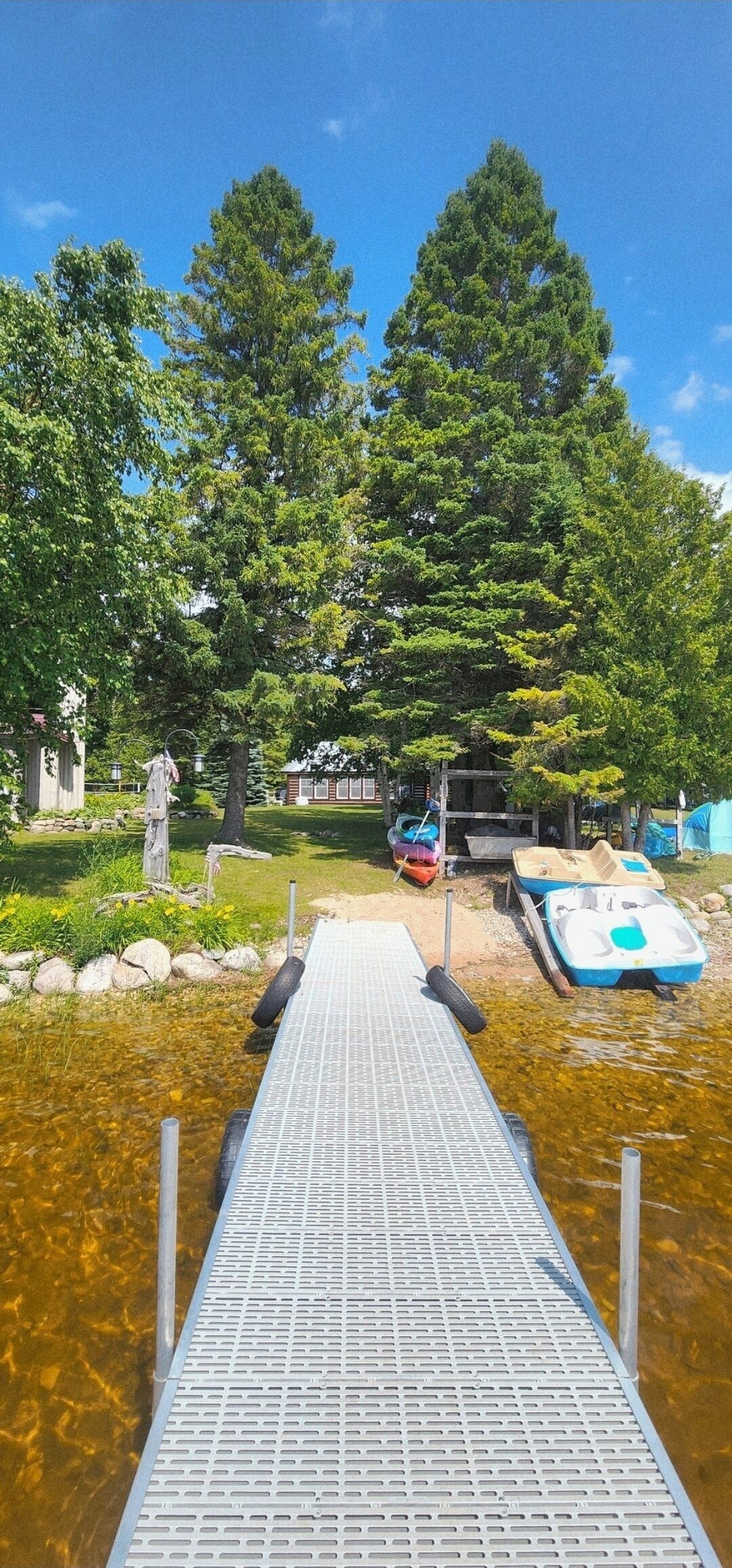 A wooden dock leading into a body of water with boats and trees in the background.