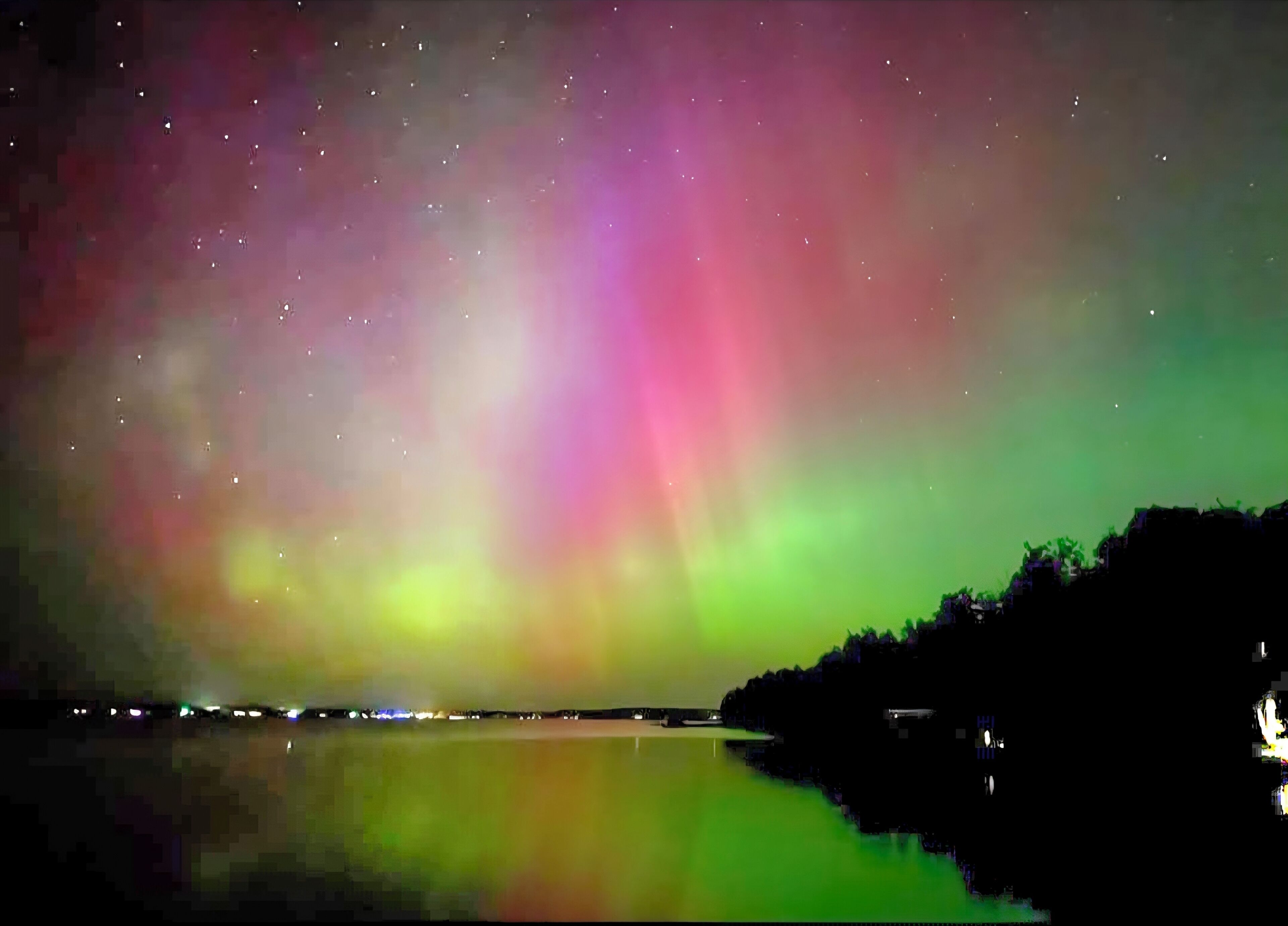 Cielo nocturno con aurora boreal vibrante sobre una masa de agua tranquila, reflejando los colores.