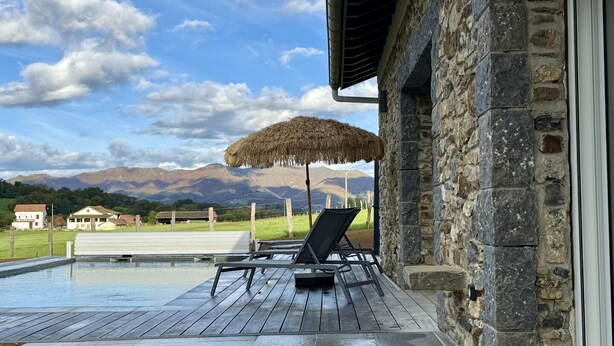 A pool area with lounge chairs and a thatched umbrella, overlooking a mountainous landscape. - IBARNIA - SUHESCUN - Gîte (SUHESCUN)